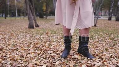 在秋天的公园里，一个兴奋的女人在投掷树叶，在缓慢的运动中玩得很开心。 靠近她的腿